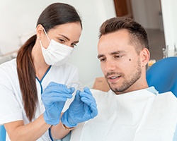 Dentist in white scrubs showing clear aligner to man in dental chair