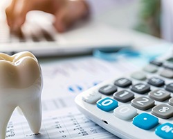 Large model tooth next to calculator on a desk with someone typing on laptop in the background